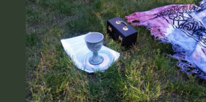 Chalice and communion host box on the grass near a blanket.